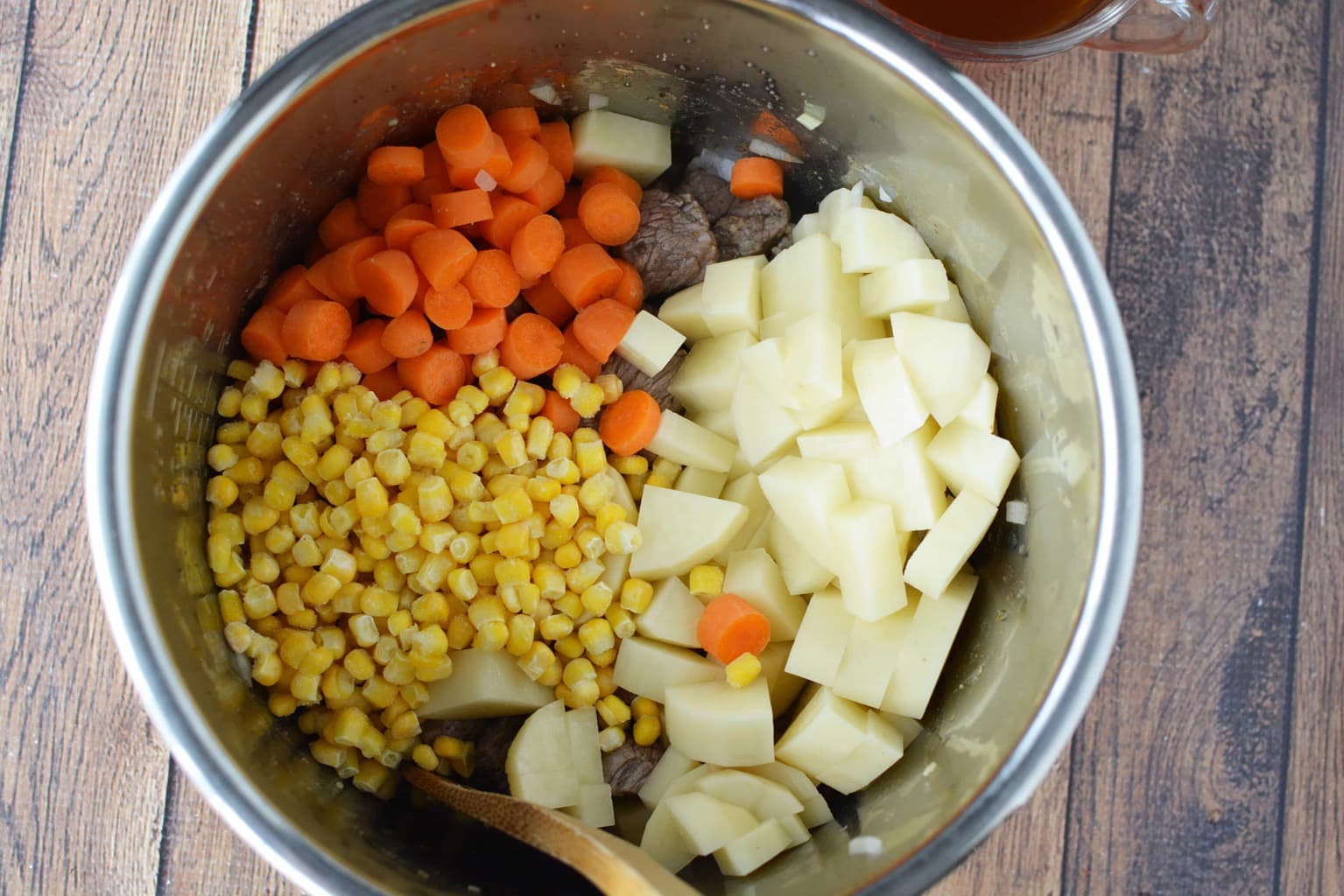 chopped carrots corn and potatoes over beef in pot