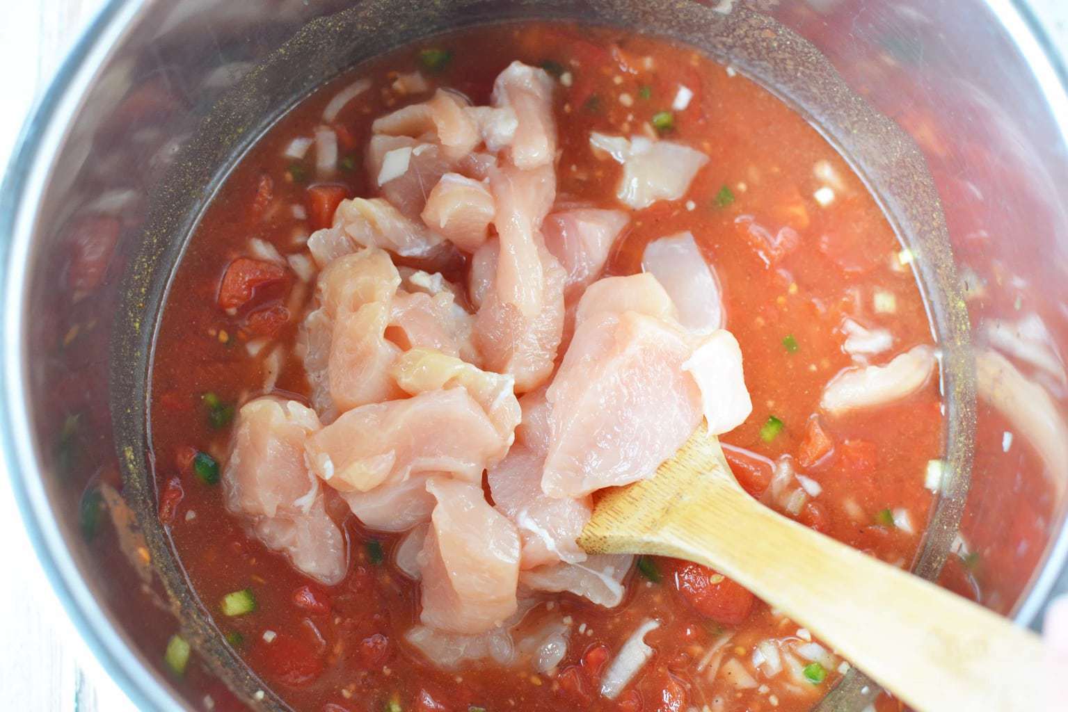 stirring in raw chicken pieces to soup in pot