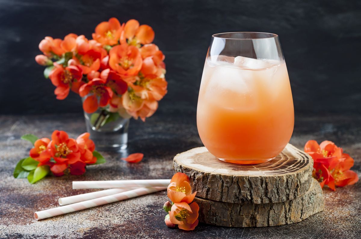 Floral pastel peach and pink brunch cocktail garnished with quince flowers over old rustic background.