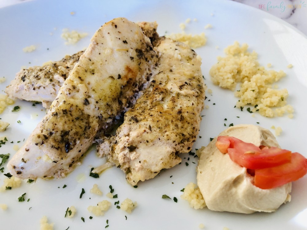 cooked chicken with a side of hummus topped with tomato on plate