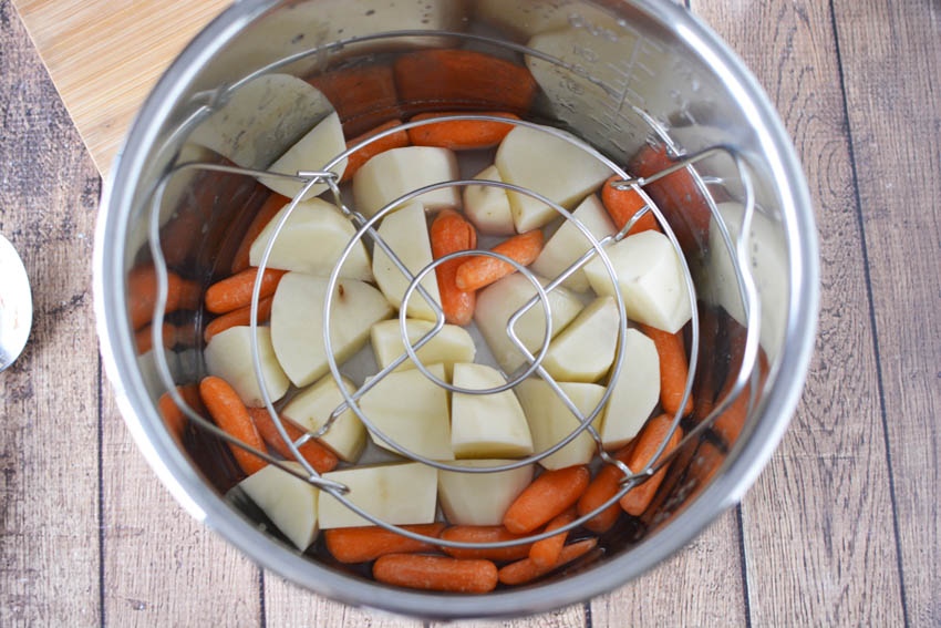 carrots and potatoes in the bottom of a pot with a trivet on top