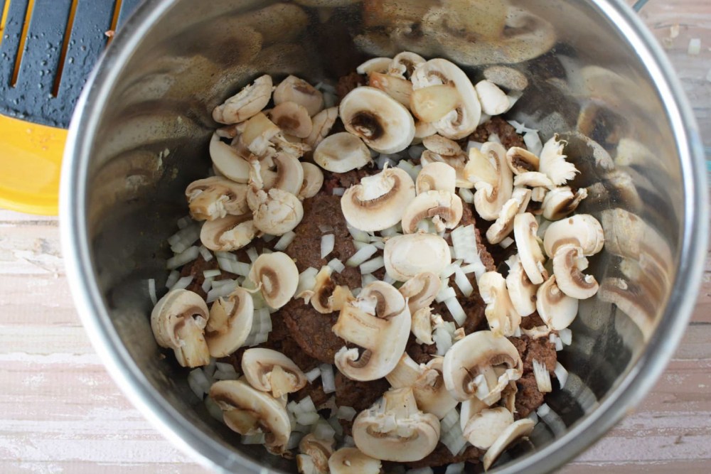 sliced mushrooms and diced onion over meat in pot