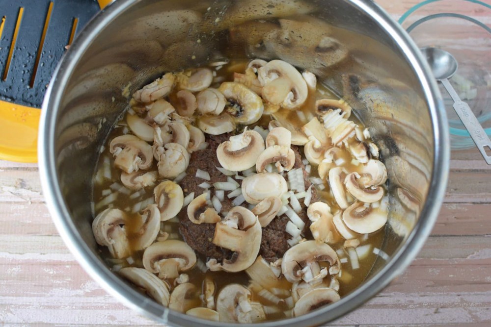 sliced mushrooms and diced onion in over meat in pot