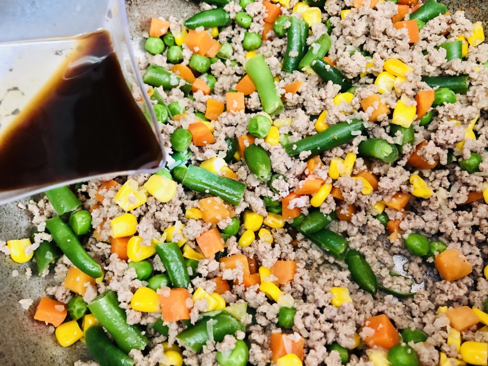 pouring Worcestershire sauce onto cooked ground beef and vegetables